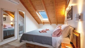 A bedroom with a sloped ceiling, a skylight, a bed with pillows and a blanket, a bedside table, and a nightstand.