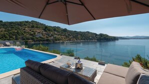 A poolside area with a view of a lake, a lounge chair, and a table with a bottle and glasses.