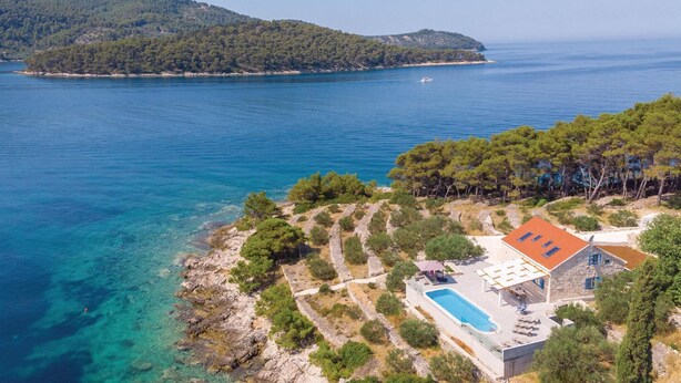 A coastal property with a swimming pool, stone pathway, and a view of the sea and a nearby island.