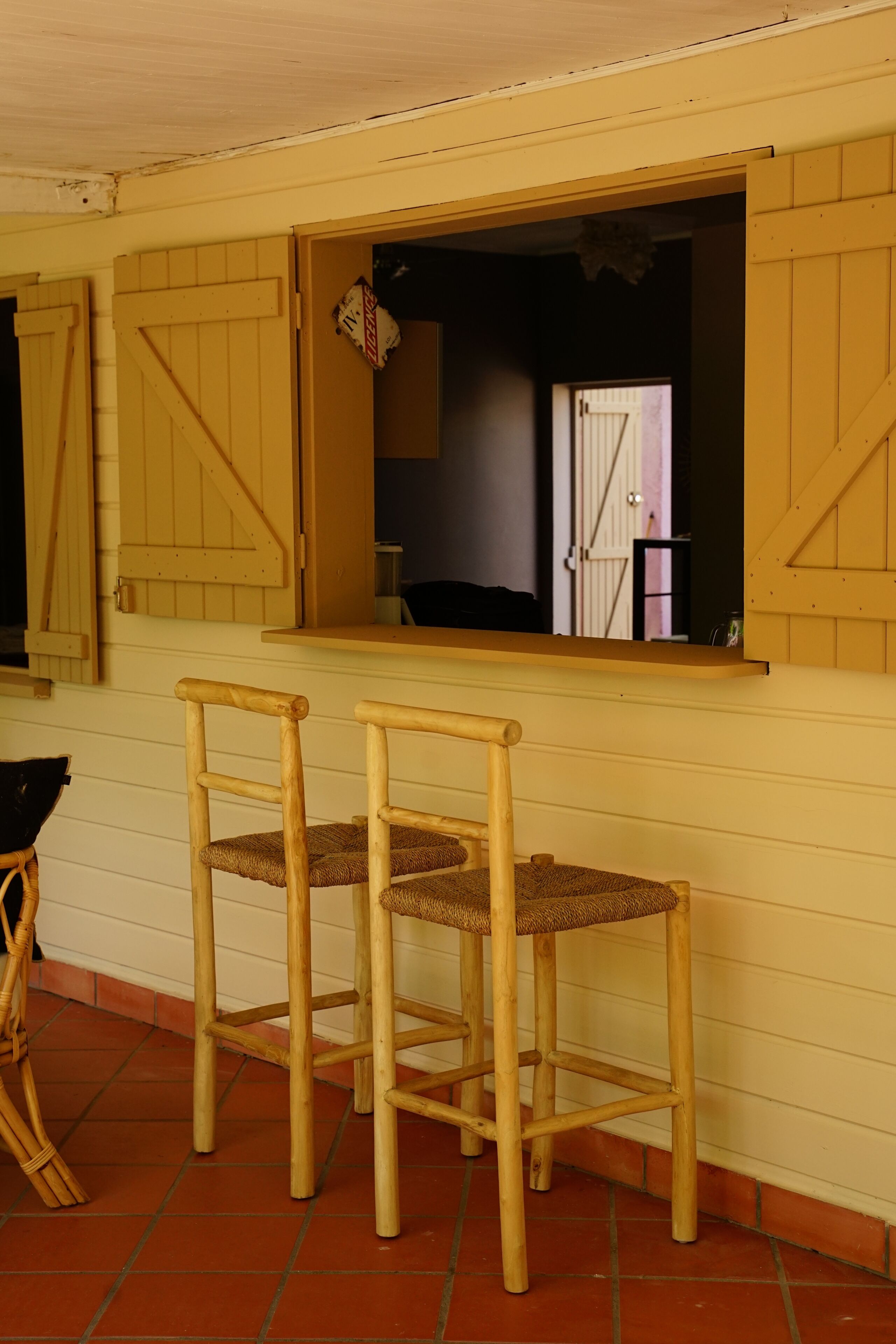 Two wooden chairs with woven seats, a window with a view of a door, and a tiled floor.