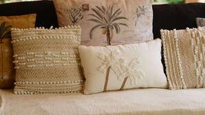 Een bank met meerdere kussens, een geweven plaid en een houten frame.