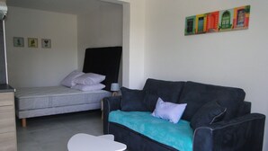 A bedroom with a bed, a sofa, and a small table. There are wall decorations and a window. - LAST MINUTE Studio N ° 5 BC (Cavalaire-sur-Mer)