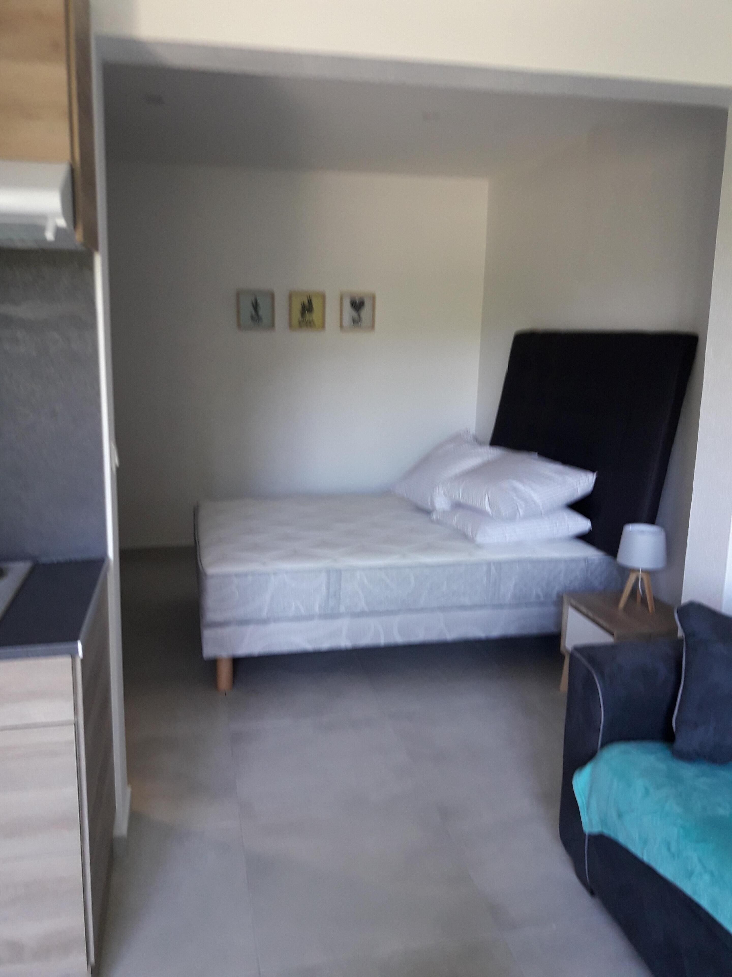 A compact bedroom with a single bed, a small bedside table with a lamp, and a sofa.