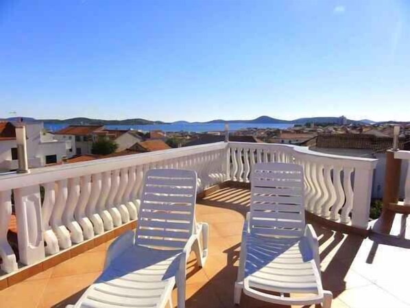 A balcony with two white lounge chairs and a view of the city and mountains.