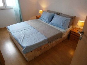 Un lit avec une couvre-lit bleue, deux oreillers, un plaid à motifs et deux lampes de chevet.