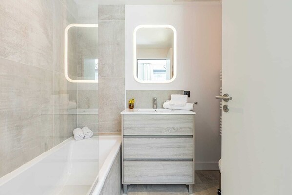 Une salle de bain moderne avec une douche à parois de verre, une baignoire blanche et un meuble-lavabo en bois avec un miroir au-dessus du lavabo.
