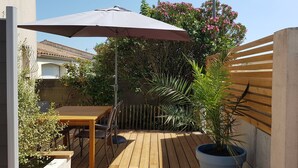 A wooden deck with a table and chairs, a large umbrella, and potted plants. - Guest house near downtown La Rochelle with heated pool (puilboreau)