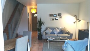A living room with a sofa, coffee table, and chairs, a staircase, and a hallway with a door leading to another room. - Guest house near downtown La Rochelle with heated pool (puilboreau)