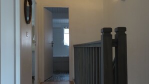 A hallway with wooden flooring, a white door on the left, and a dark railing on the right. - Guest house near downtown La Rochelle with heated pool (puilboreau)