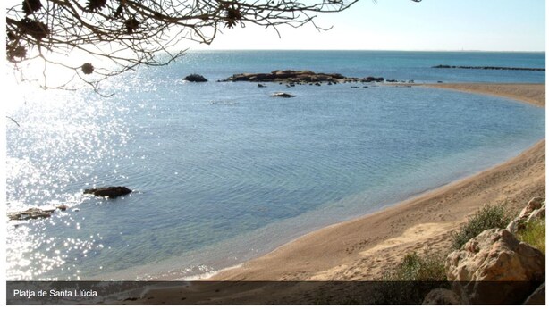 Une scène de plage avec une eau claire, un rivage sablonneux et des affleurements rocheux.