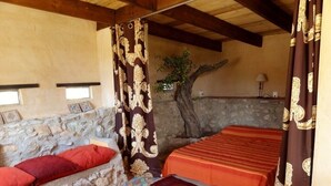 Une pièce avec un mur en pierre, un arbre et un lit recouvert d’une couverture orange.
