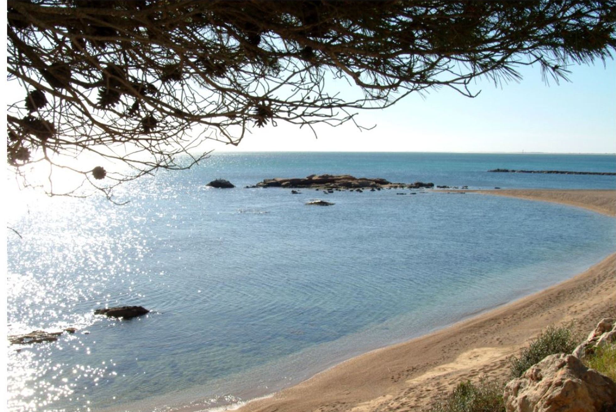 A beach scene with clear water, a sandy shore, and rocky outcrops.
