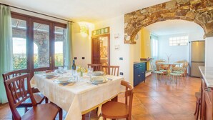A dining area with a stone archway, a kitchen in the background, and a view through a window.