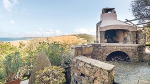 A stone-built outdoor oven with a view of the beach and hills in the background.