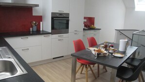 Cocina moderna con armarios blancos, encimera negra y sillas rojas. Hay una mesa de comedor con platos, tazas y un hervidor.