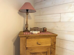 A wooden nightstand with a lamp, a small table with a checkered cloth, and a drawer. - Centre Cauterets, appartement 72m2 pr 7 personnes (Cauterets)