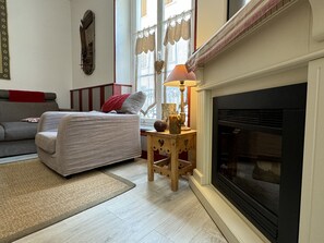 A cozy living room with a fireplace, a sofa, a small wooden side table, and a rug. - Centre Cauterets, appartement 72m2 pr 7 personnes (Cauterets)