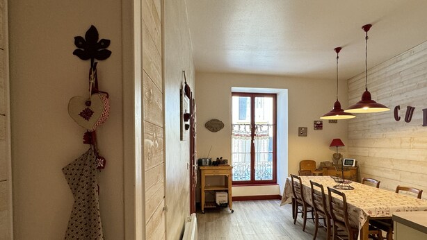 A narrow hallway leading to a dining area with a wooden floor, a window with lace curtains, and a table set for dining. - Centre Cauterets, appartement 72m2 pr 7 personnes (Cauterets)