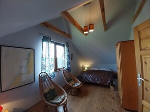 Cozy attic bedroom with a large bed, wicker chairs, and a wooden wardrobe, perfect for a relaxing retreat.