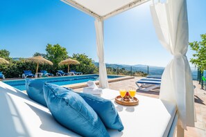 A poolside lounge with a view of the pool, blue lounge chairs, and a breakfast tray with drinks.
