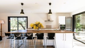 Una cocina moderna con una isla grande, taburetes de bar, iluminación colgante y vistas al exterior.