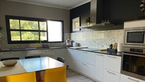 Una cocina moderna con armarios blancos, un ventanal grande y una zona de comedor con sillas amarillas.
