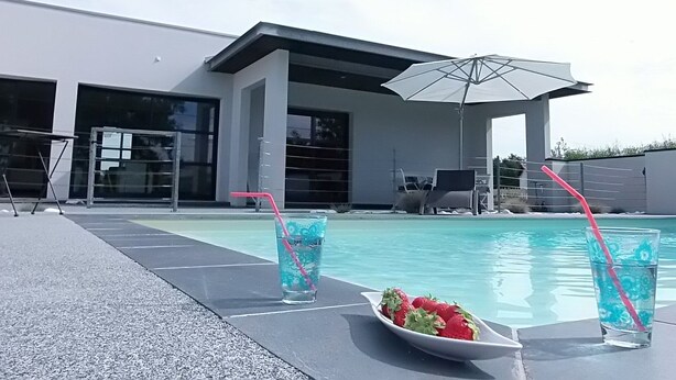 Un área de piscina exterior moderna con piscina azul cristalina, sillones de descanso y sombrillas.