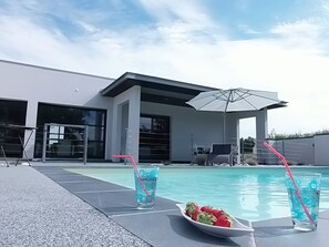 Een modern zwembadterras met een helderblauw zwembad, ligbedden en parasols.