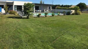 Un edificio moderno con piscina, rodeado de césped cuidado y pequeñas palmeras.