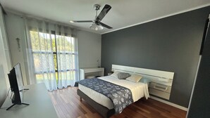 Un dormitorio moderno con cama, mesitas de noche, un escritorio con computadora y un ventilador de techo.