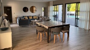 Una sala moderna con comedor, un sofá, una mesa de centro y un gran ventanal con cortinas.