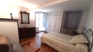Een slaapkamer met een bed, een stoel, een dressoir, een spiegel en een kast.