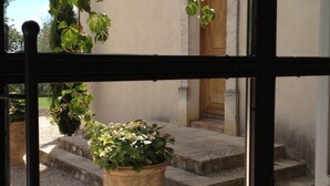 A view through a window of a building with a stone staircase leading to a wooden door, surrounded by gravel and potted plants. - LA BASTIDE D'ANDRÉA, PRESTIGIOUS VILLA FOR 12 PEOPLE, NOT OVERLOOKED (Martignargues)
