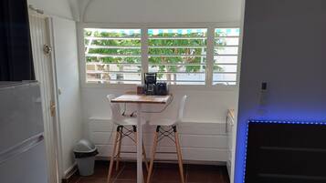 Una habitación pequeña con una mesita, dos sillas, una cama y un ventanal con persianas.