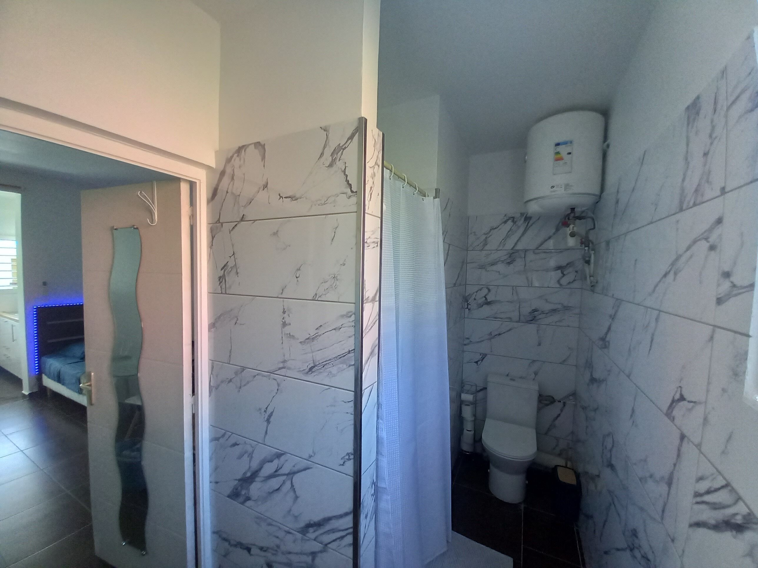 A bathroom with marble tiles, a toilet, and a shower enclosure.