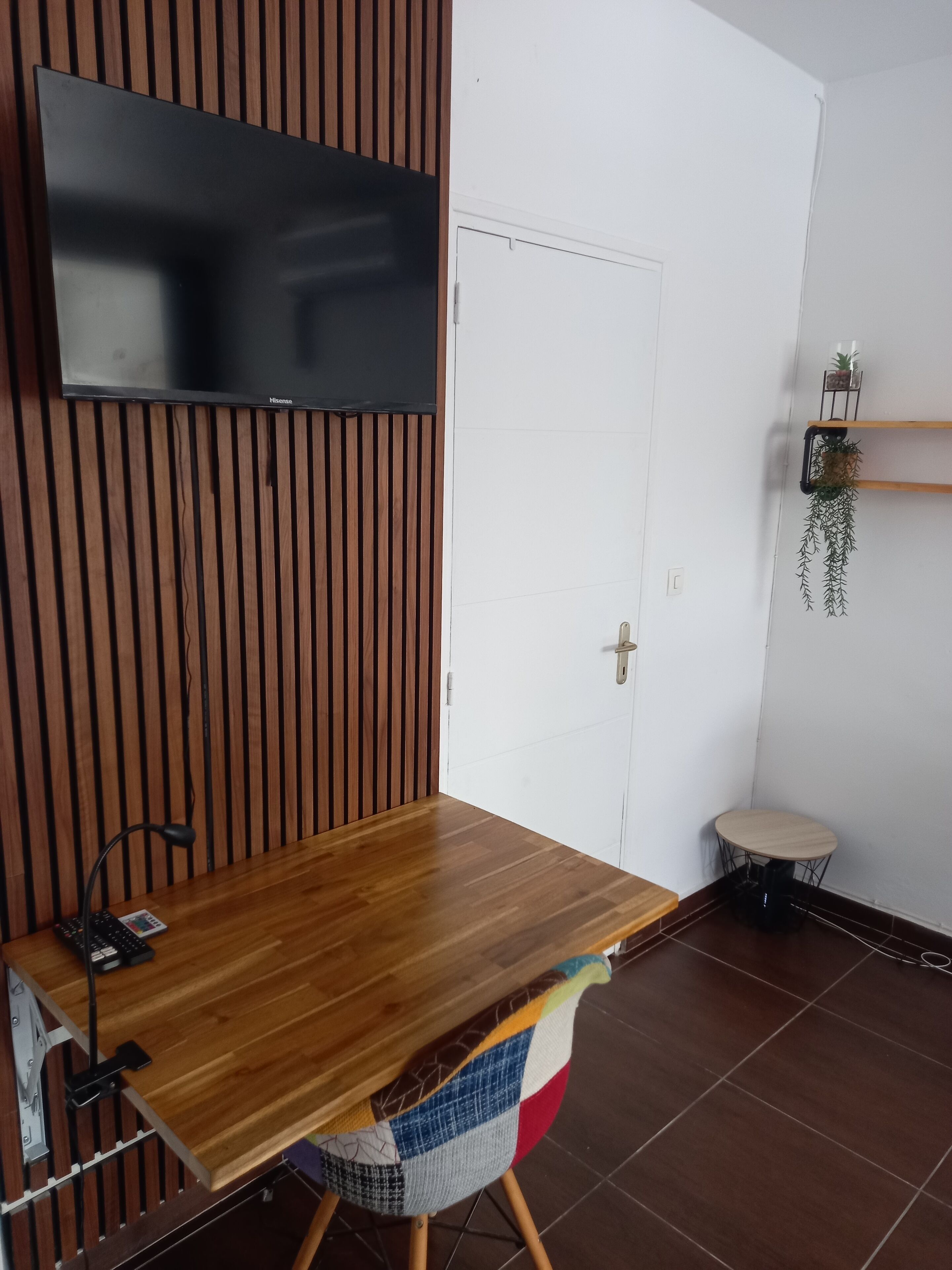 Moderni huone, jossa on puinen ruokapöytä, puiseen seinäpaneeliin kiinnitetty televisio, valkoinen ovi ja pieni pyöreä pöytä tuolilla.