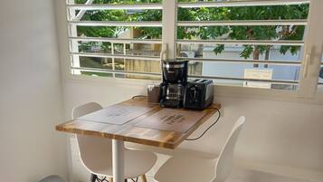 Un pequeño comedor con una mesa y sillas, una cafetera y una ventana con persianas.