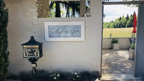 A sign with 'Le Petit de Gianni' written on it, a lantern with 'LETTERS' on it, and a gravel path leading to a building entrance.