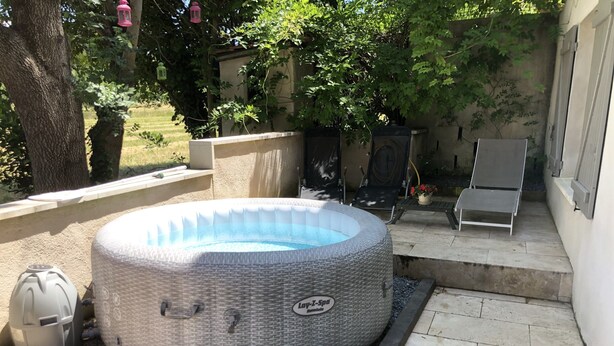 A hot tub in a backyard with a stone pathway, a trash can, and a flower pot.