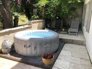 A hot tub in a backyard with a stone pathway, a trash can, and a flower pot.