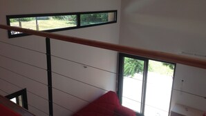 Ein modernes Interieur mit einer Treppe, einem roten Sessel und Blick auf einen Garten durch große Fenster.