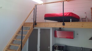 Ein Schlafzimmer im Loft-Stil mit einer Holztreppe, einem roten Bett und einer kleinen Küchenzeile.