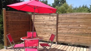 Eine Holzterrasse mit einem runden Tisch, vier roten Stühlen, einem Sonnenschirm und einem Holzzaun.