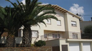 A two-story building with a stone wall in front, a balcony with a metal railing, and a garage with a white door. - BEAUTIFUL APARTMENT for 4/6 people in the center of ROSES, 250 mt from the beach (Roses)