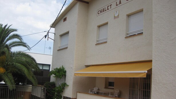 A building named "CHALET LA CUAVO" with a tiled patio, outdoor seating, and a palm tree. - BEAUTIFUL APARTMENT for 4/6 people in the center of ROSES, 250 mt from the beach (Roses)