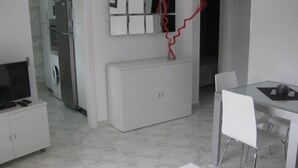 A modern kitchen with a built-in oven, a microwave, and a refrigerator. There is a dining area with a glass table and white chairs. - BEAUTIFUL APARTMENT for 4/6 people in the center of ROSES, 250 mt from the beach (Roses)