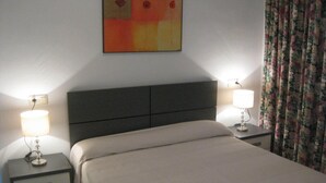 A hotel room with a bed, two bedside tables with lamps, a wall-mounted artwork, and a floral curtain. - BEAUTIFUL APARTMENT for 4/6 people in the center of ROSES, 250 mt from the beach (Roses)
