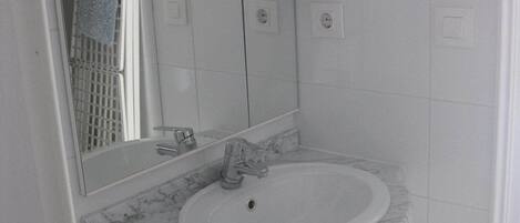Une salle de bain avec un lavabo blanc, un comptoir en marbre et un miroir au-dessus. Un porte-serviettes est fixé au mur et, sous le lavabo, on trouve un meuble blanc.