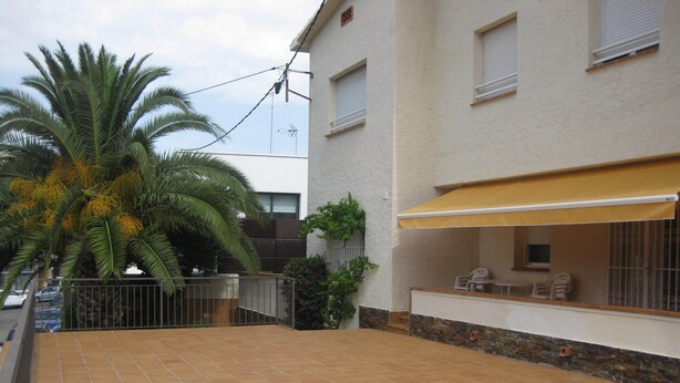 Un'area patio con pavimento piastrellato, una palma, una zona salotto coperta e un edificio con finestre e un balcone.