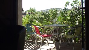 En balkon med et bord og stole, udsigt over en have og en bakke.